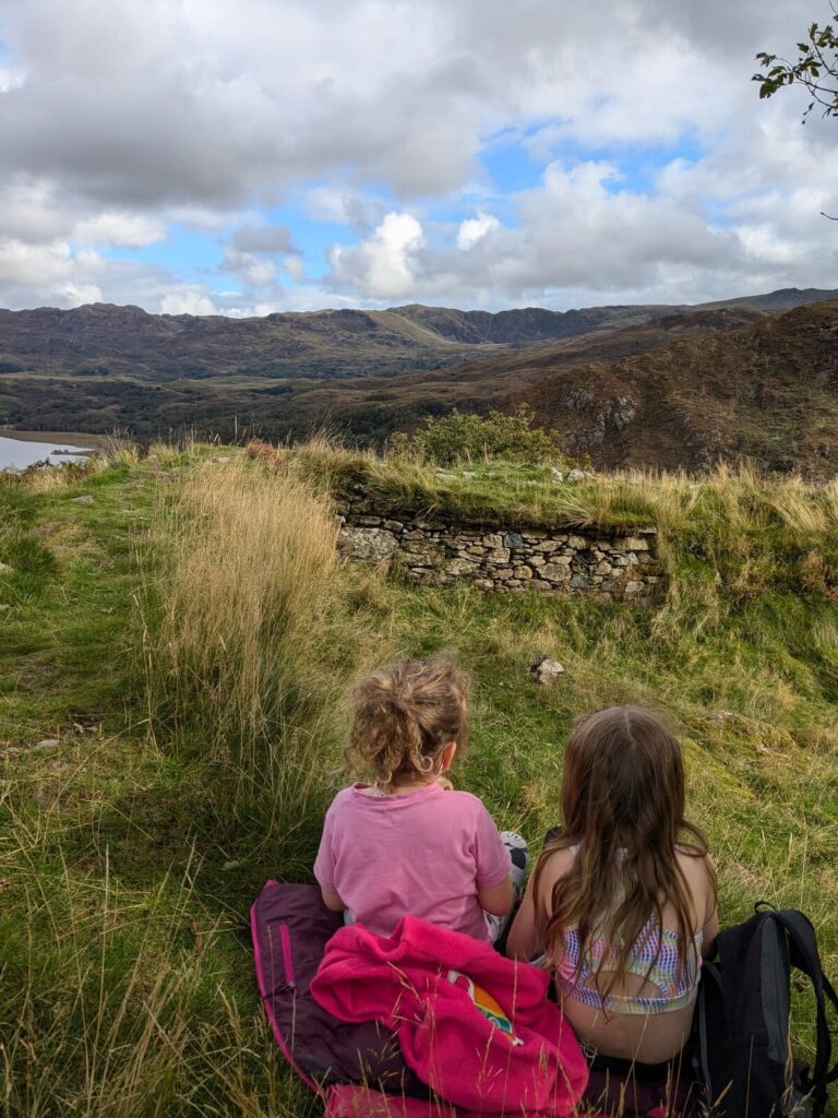 Two children sitting at the top of Dinas Emrys hillfort near Beddgelert with mountain views behind them