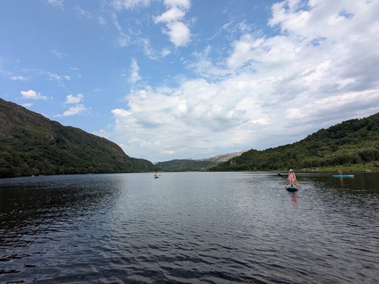 Child paddleboarding on Llyn Dinas lake near Beddgelert, surrounded by mountains in Eryri Snowdonia