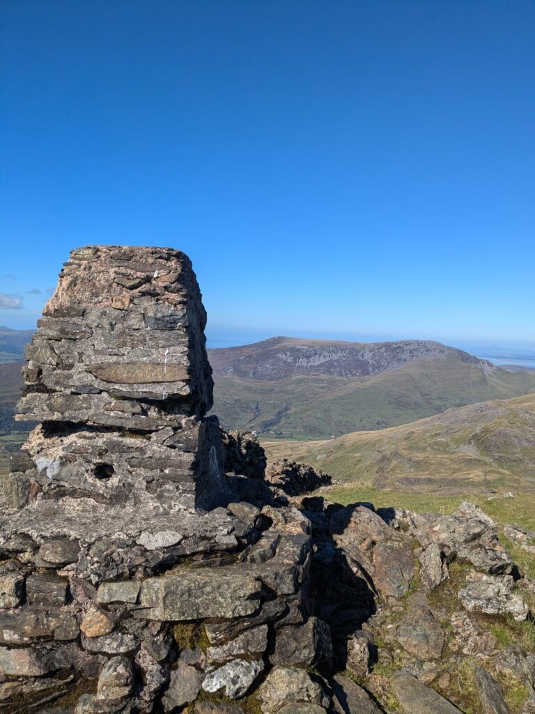 The OS trig point on the summit of Moel Hebog, with Mynydd Mawr visible in the distance