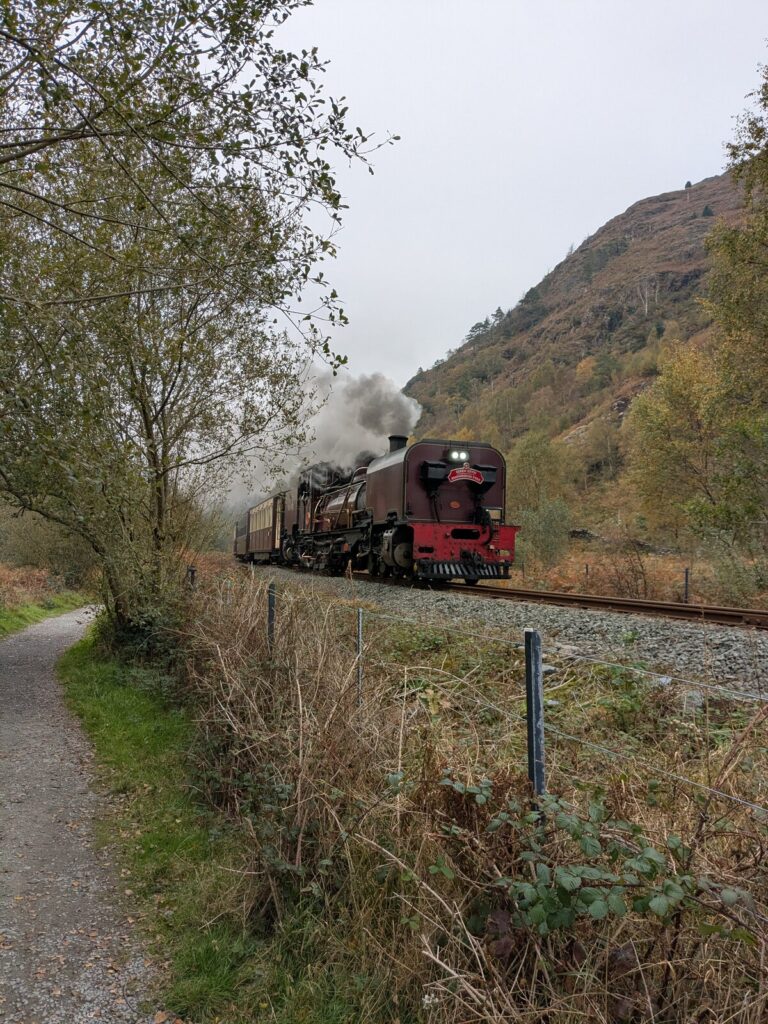 Steam train passing the Fisherman's Walk footpath in Beddgelert village, Eryri Snowdonia